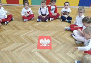 Dzieci siedzą w kole, w środku leży duże godło Polski.